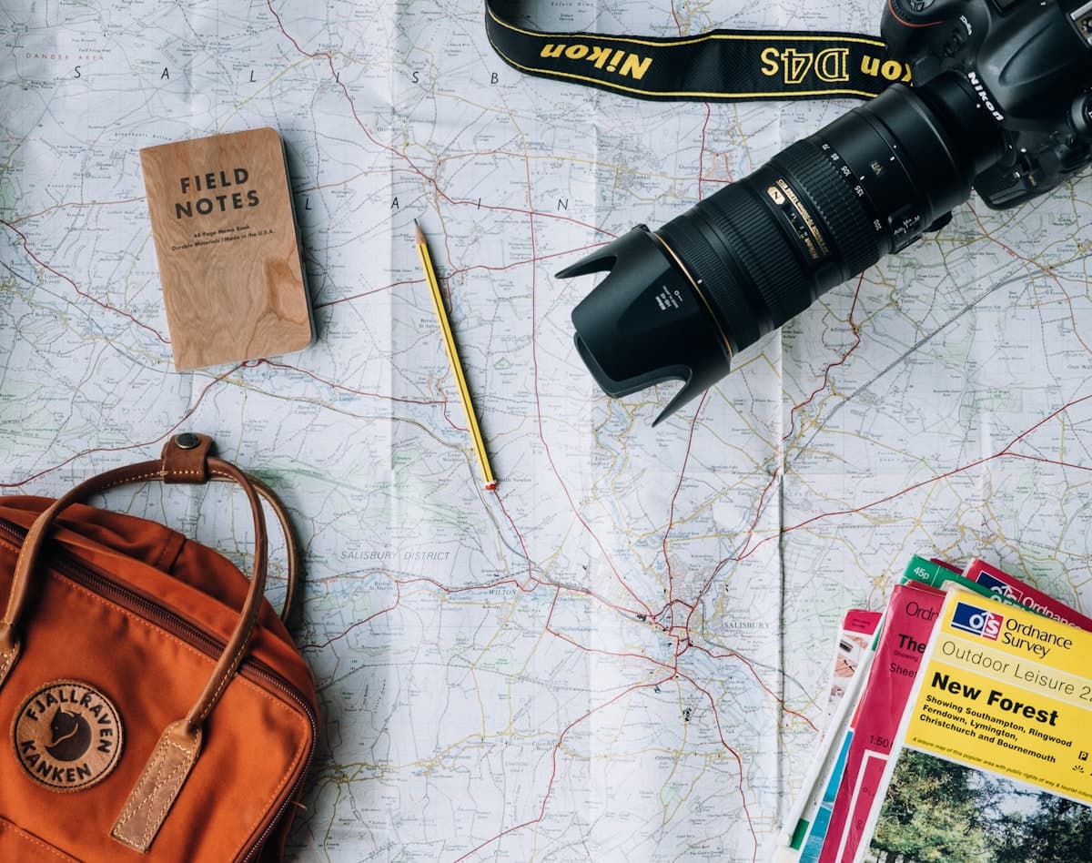 Landkarte mit Notizbuch, Kamera und Rucksack auf einem Tisch — Symbol für die Planungsphase